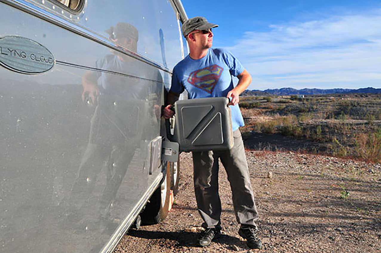 man filling up a water jug next to trailer