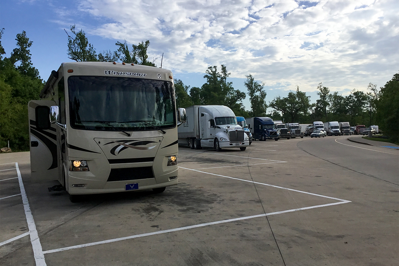 Class A parked next to several semi-trucks at a rest stop.