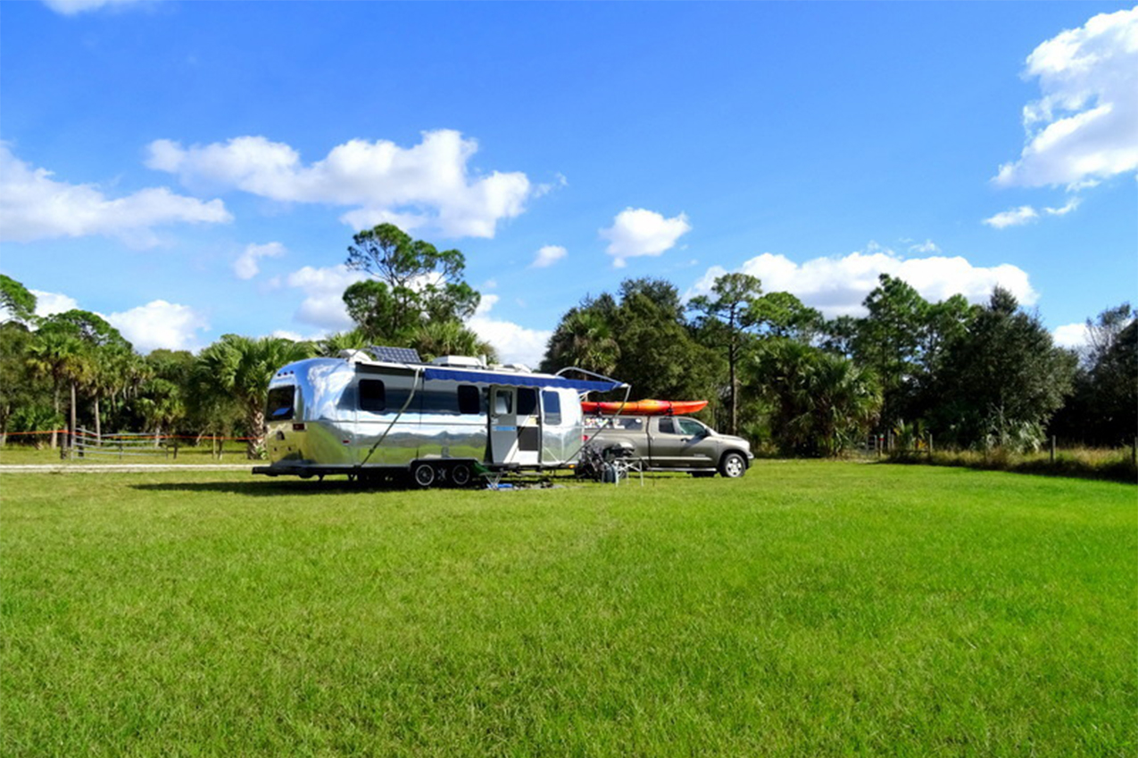 Shiny Airstream and truck with kayak on top parked in a green field.