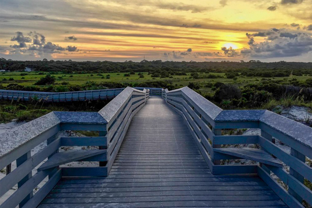 Sunset over boardwalk and sand dunes.