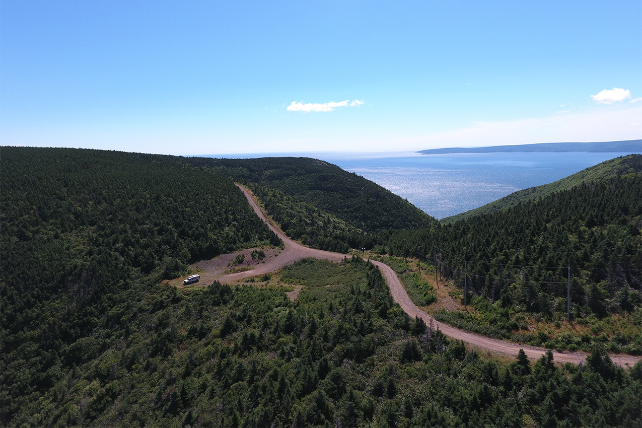 Truck camper parked on a lonely road surrounded by trees and a body of water in the background.