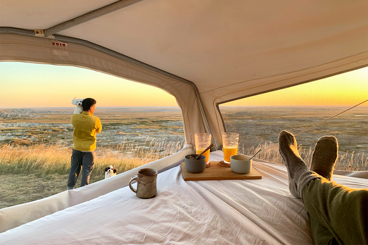 Person holding dog standing outside camper during sunset