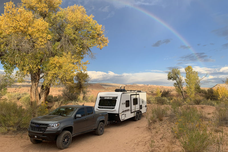 Truck towing a travel trailer with a rainbow across the blue sky.