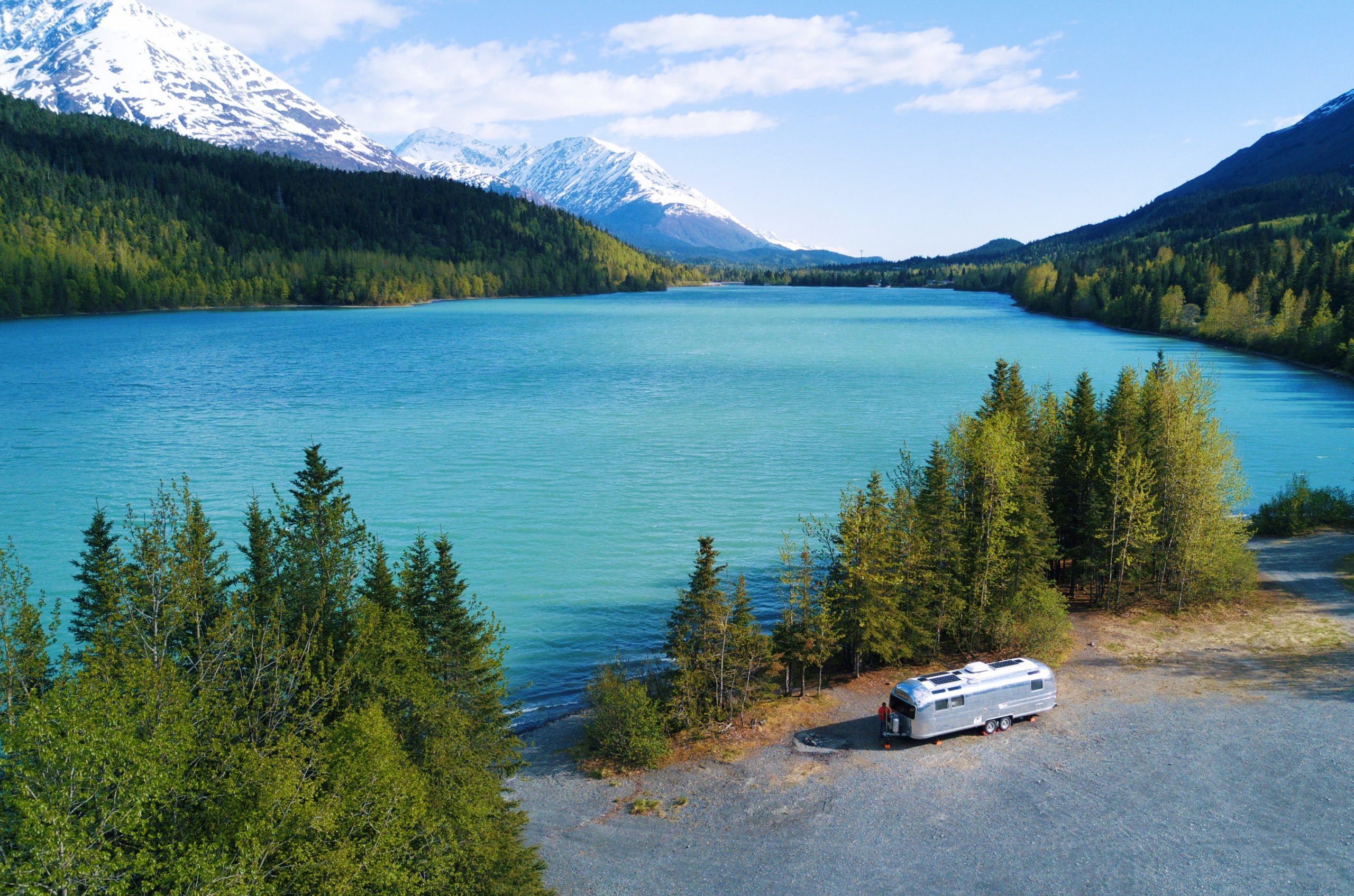 RV parked in front of blue water and large mountains