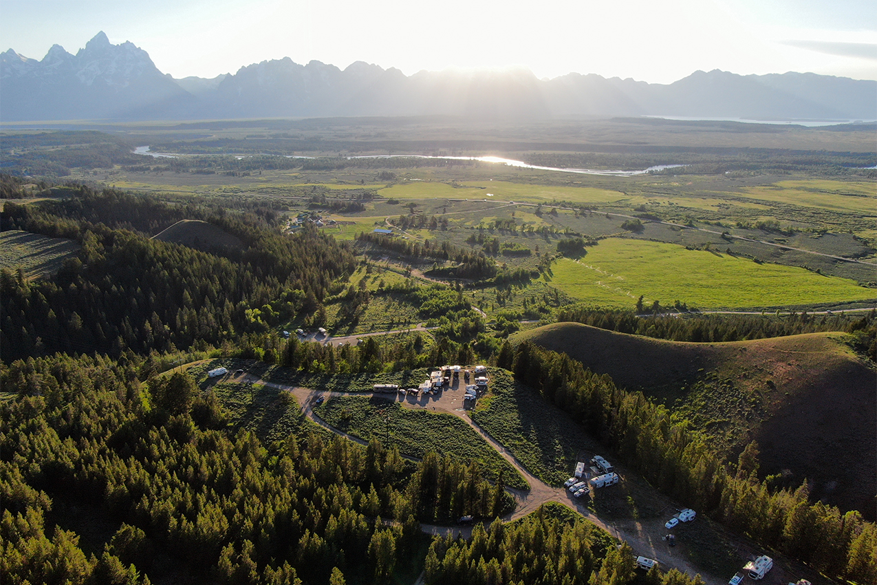 Aerial view of RVs parked in a forest and in front of mountains.