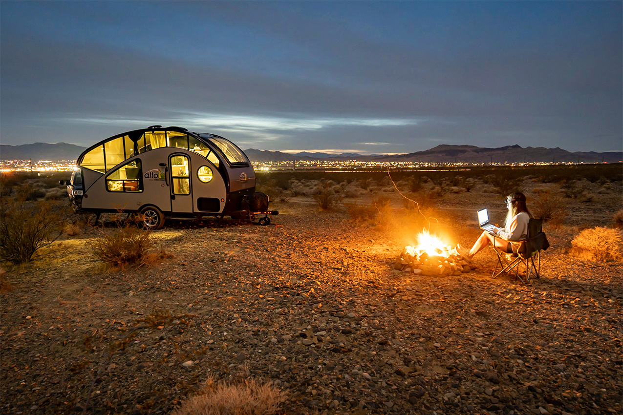 Teardrop camper and person sitting in front of campfire.