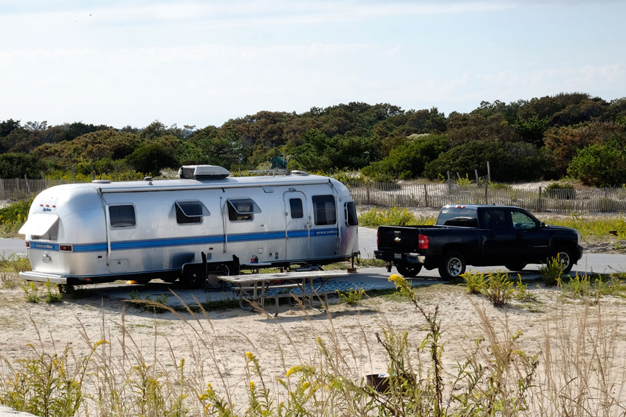 RV and truck parked near sand dunes.