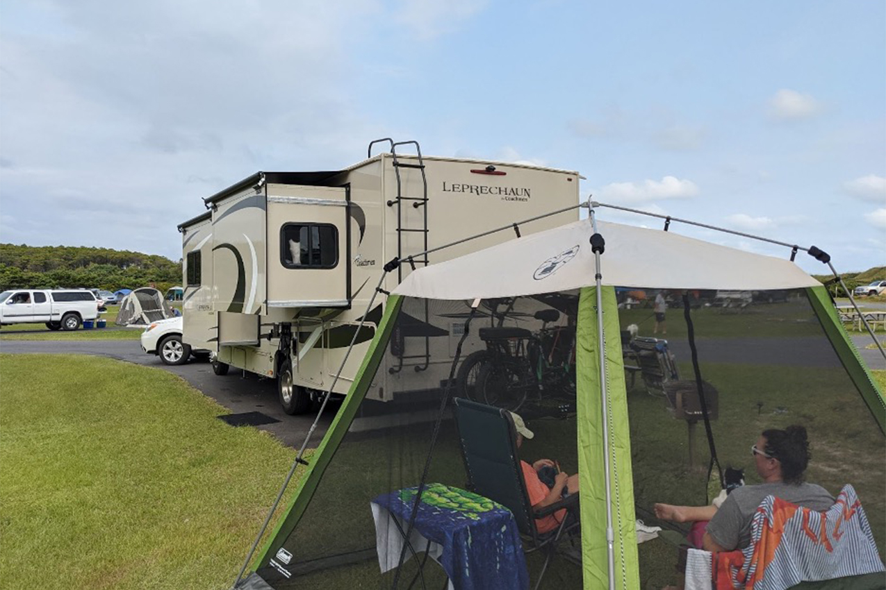 Couple sitting inside a screened tent behind their RV.
