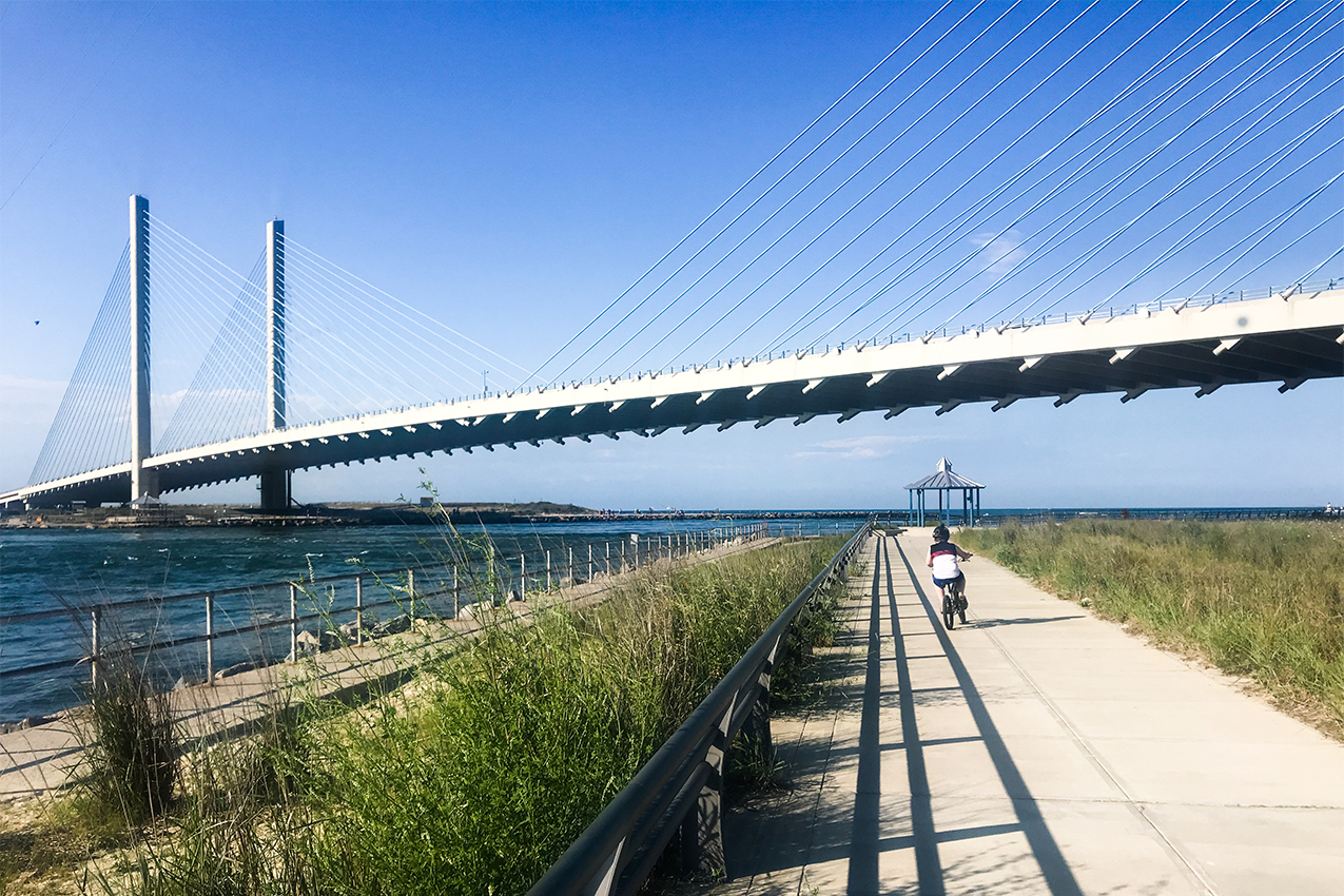 Cyclist on greenway next to a beach and bridge.