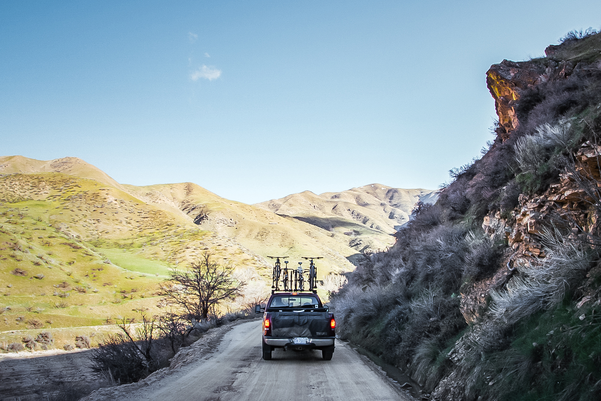Truck with bikes on roof driving down gravel wall next to rock wall.