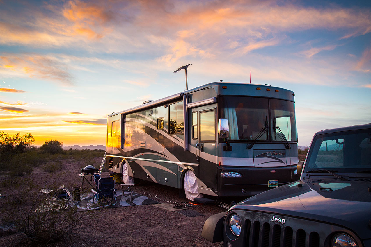 Class A and Jeep parked in the desert at sunset.