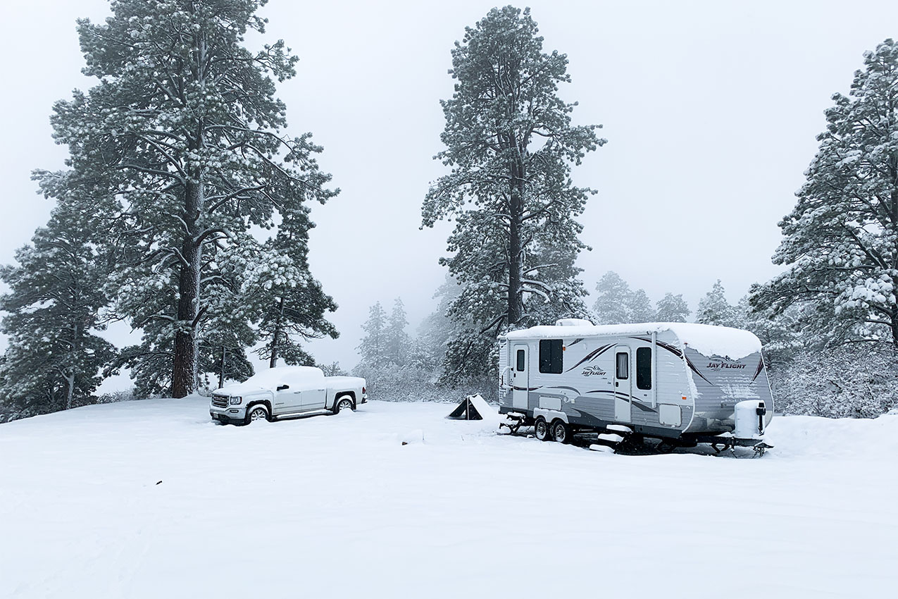 Truck and travel trailer parked in the snow in the woods.