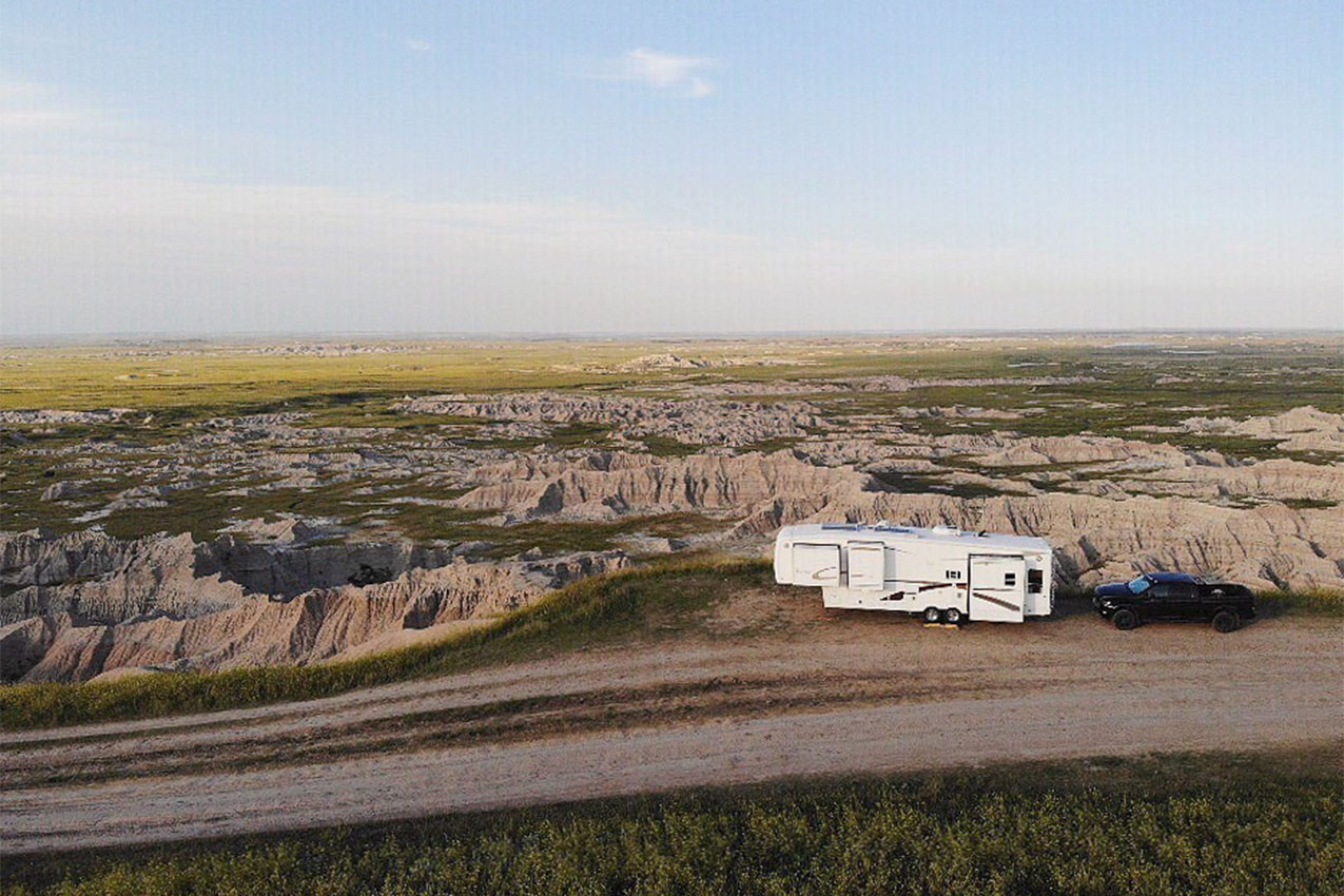 Fifth wheel parked on the edge of a cliff next to a dirt road.
