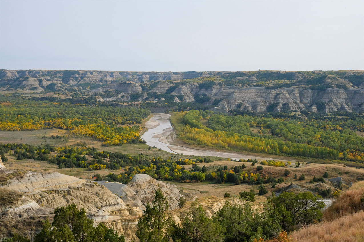 River running through a fall colored field surrounded by montains.
