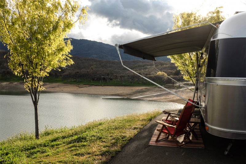 RV with awning and camp chairs out next to a lake.