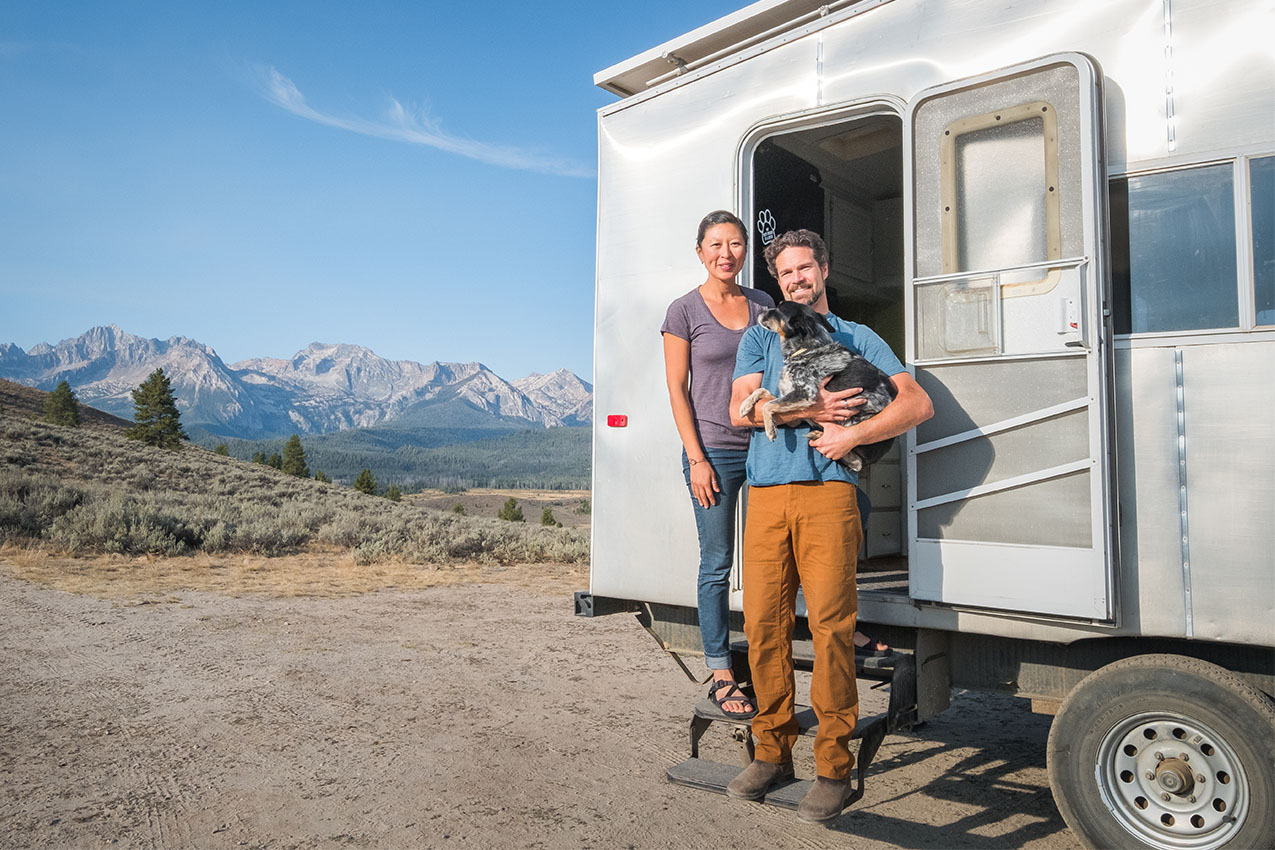 A couple and a dog standing in front of their silver RV.
