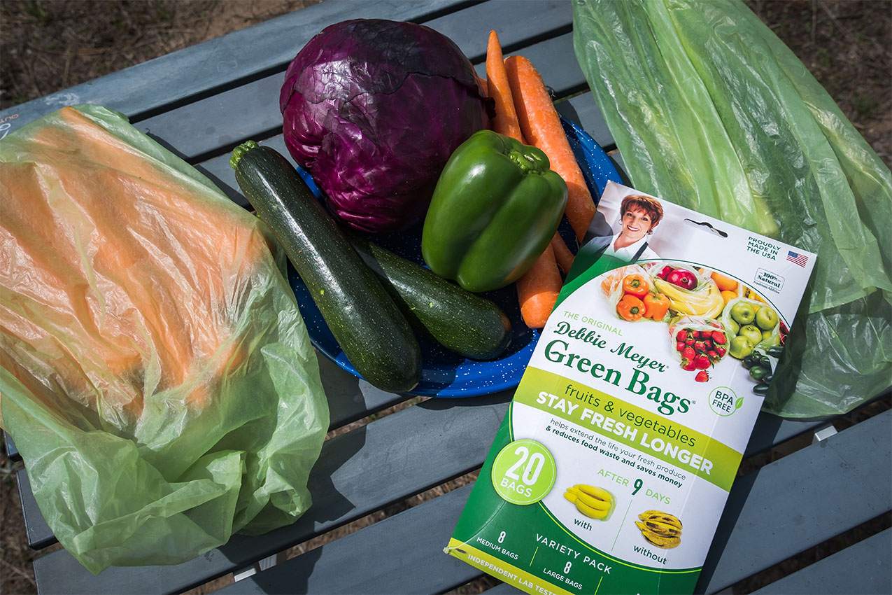 Vegetables in two green bags and a plate of fresh vegetables.