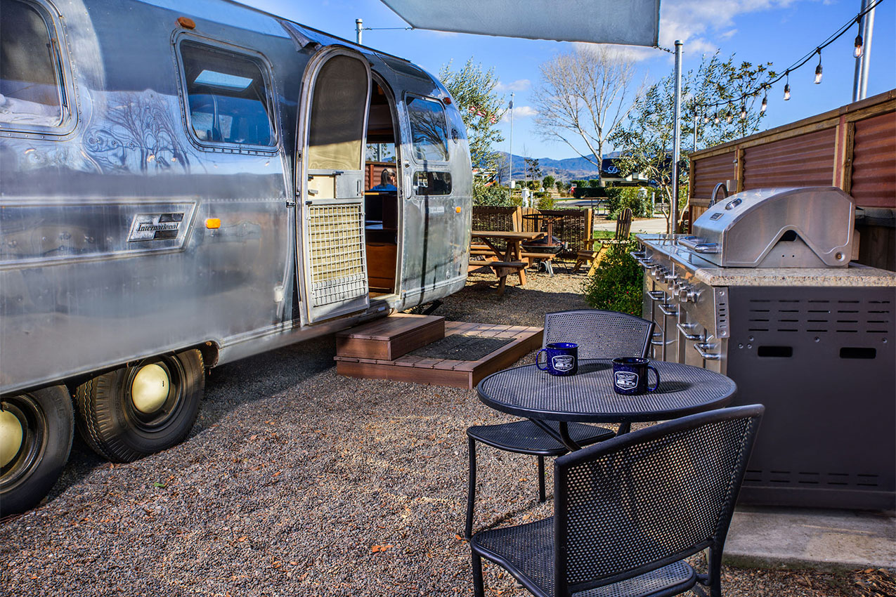 Airstream parked next to a outdoor grill and table.