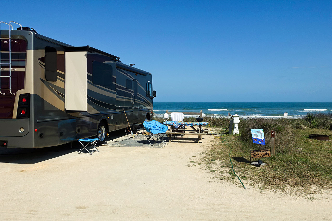 Class A with outdoor seating set up at campsite in front of ocean.