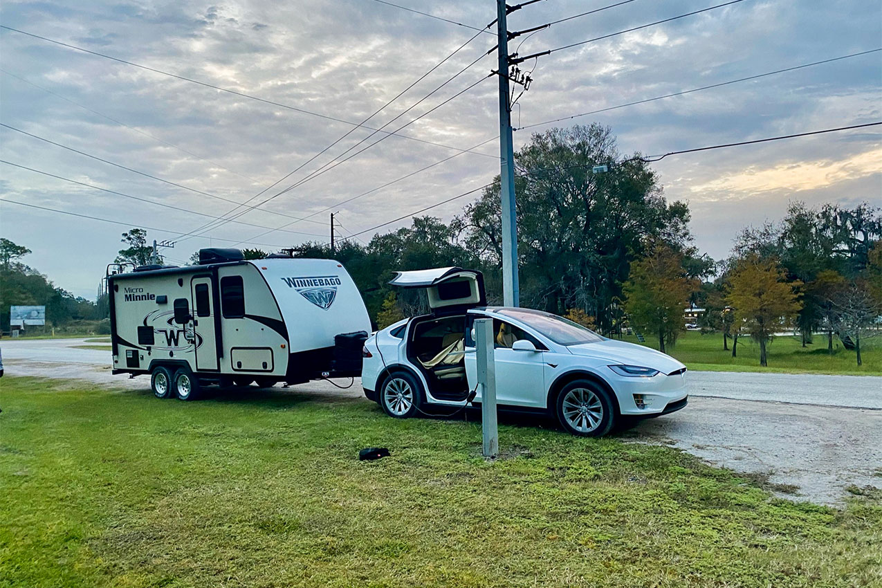 Tesla car towing RV charging at a station.