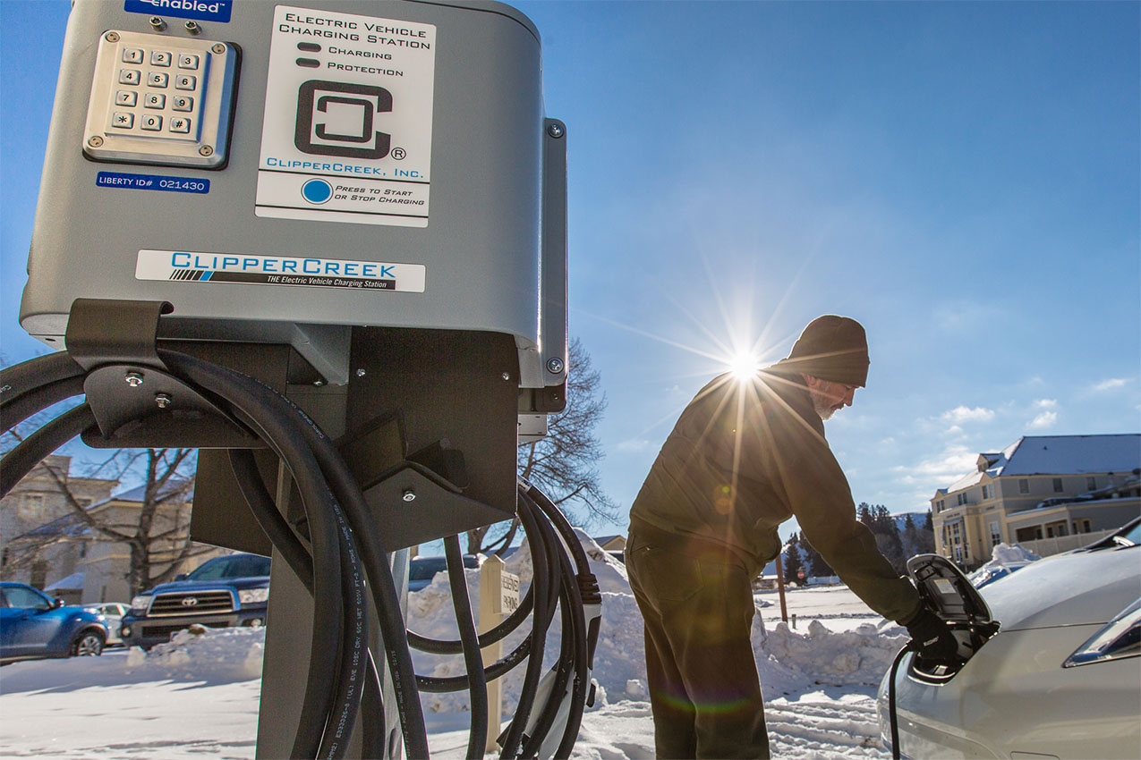 A man charging his electric vehicle in the snow at a charging station.