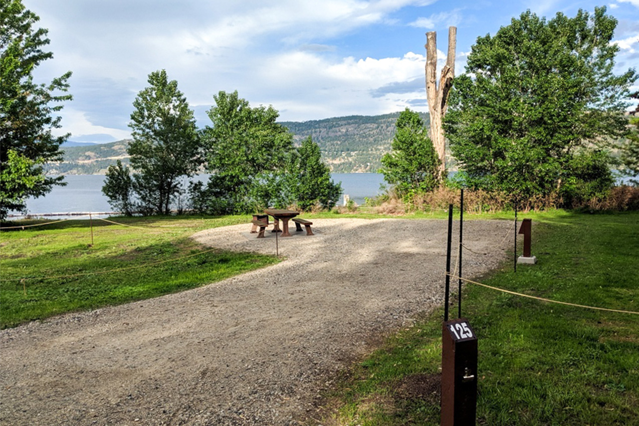 Gravel RV campsite with a picnic table in front of a lake.