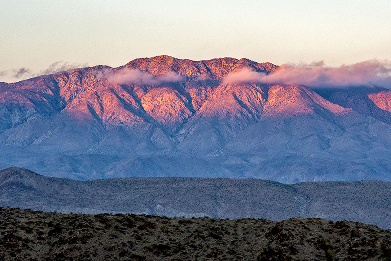 Close up of pink mountains and clouds in front of it.