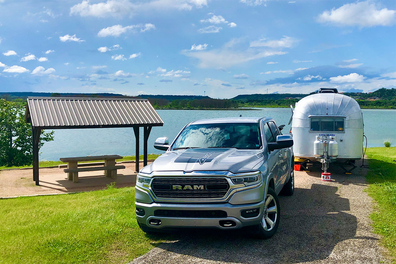 Truck and Airstream parked in front of a lake next to a covered picnic table.