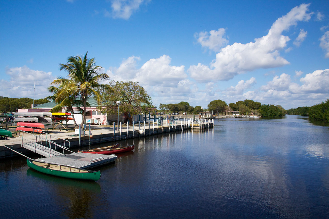 A few canoes tied to a dock on a blue river with palm trees.