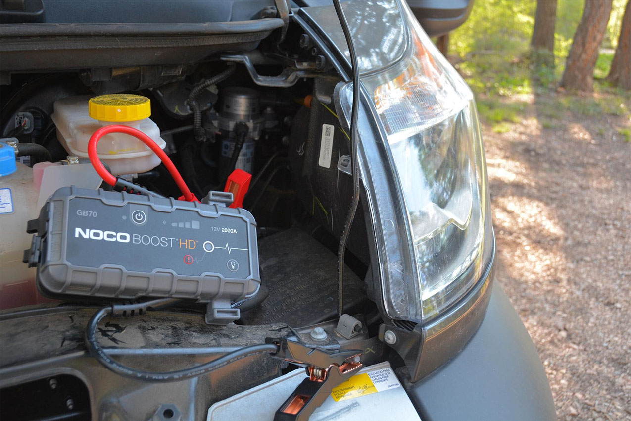 A rectangular jump starter clamped to van batteries.