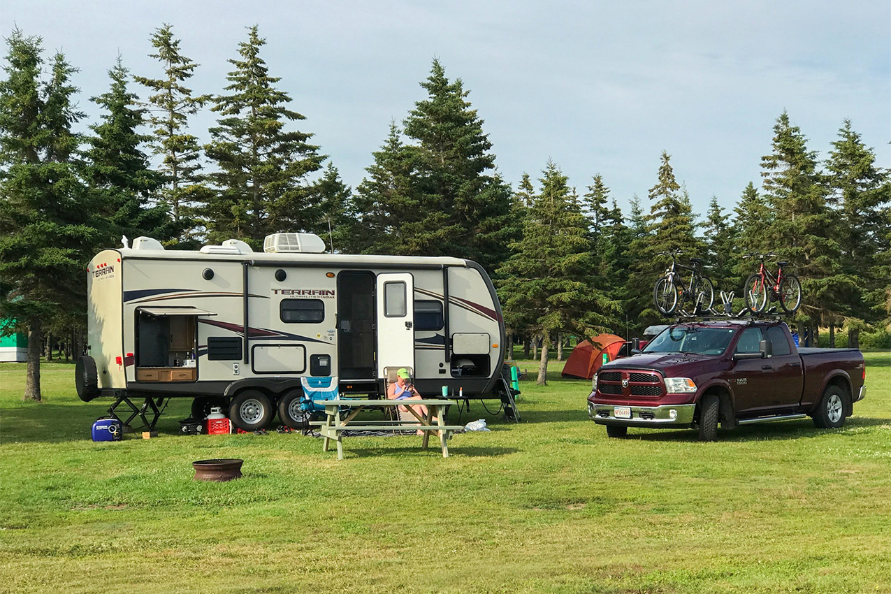 Woman sitting in front travel trailer, picnic table, and truck.