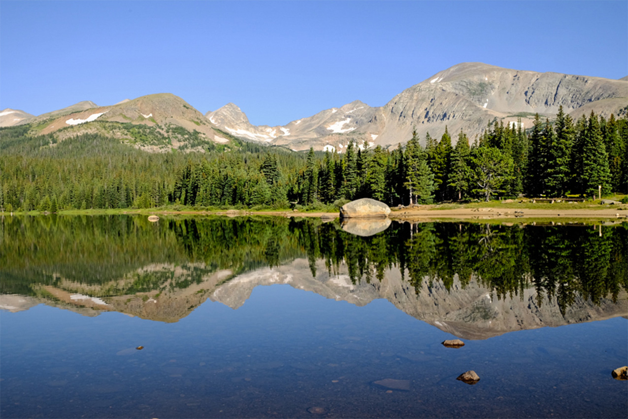 Mountains lined with trees along the shore of a blue lake.