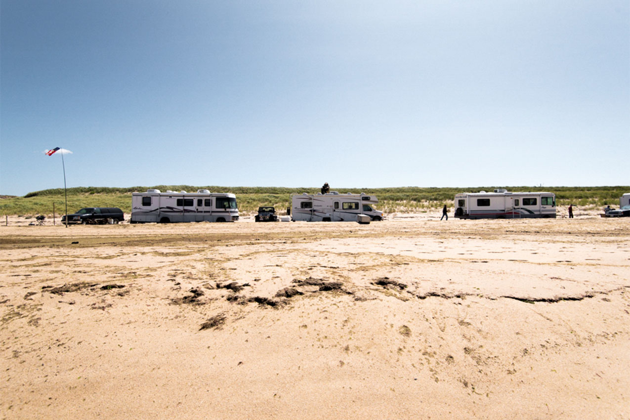 Three RVs parked on a sandy beach.
