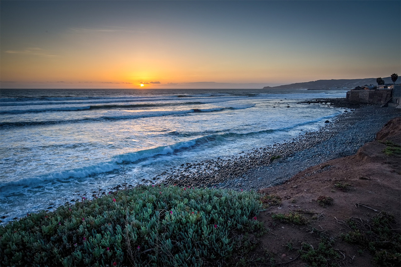 Sandy beach with the sun setting on the horizon.