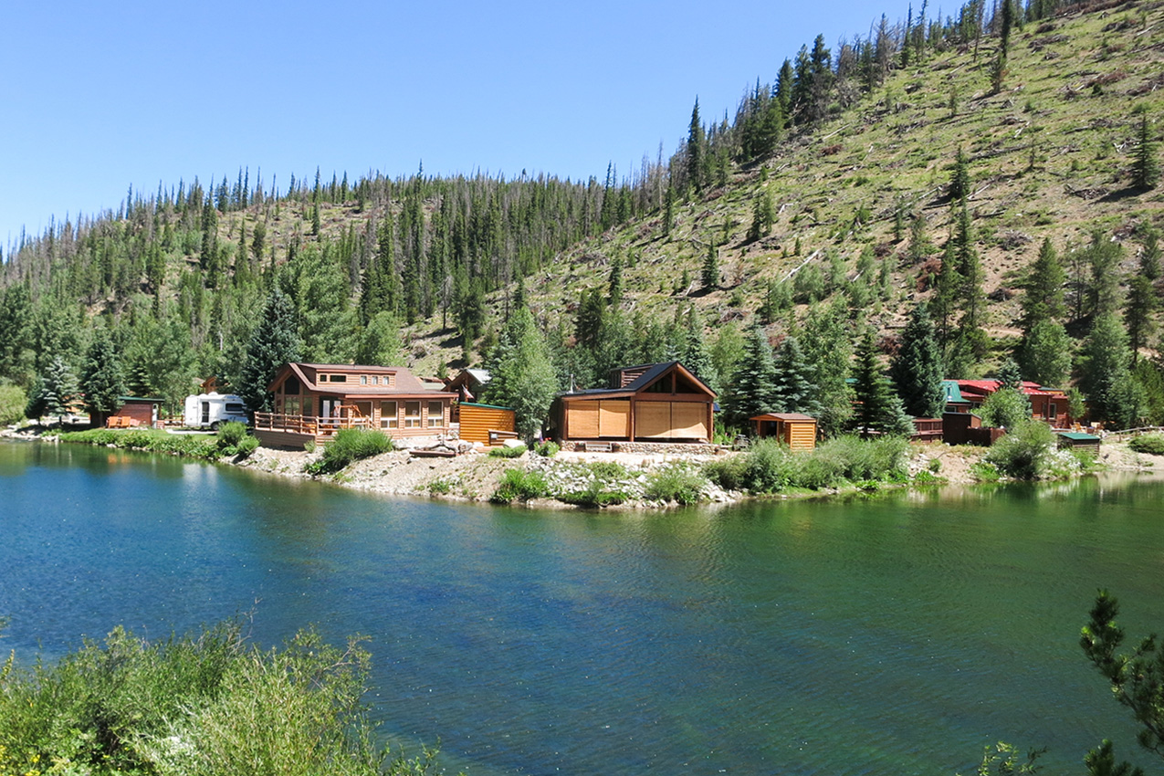 River running in front of several cabins in the mountains.
