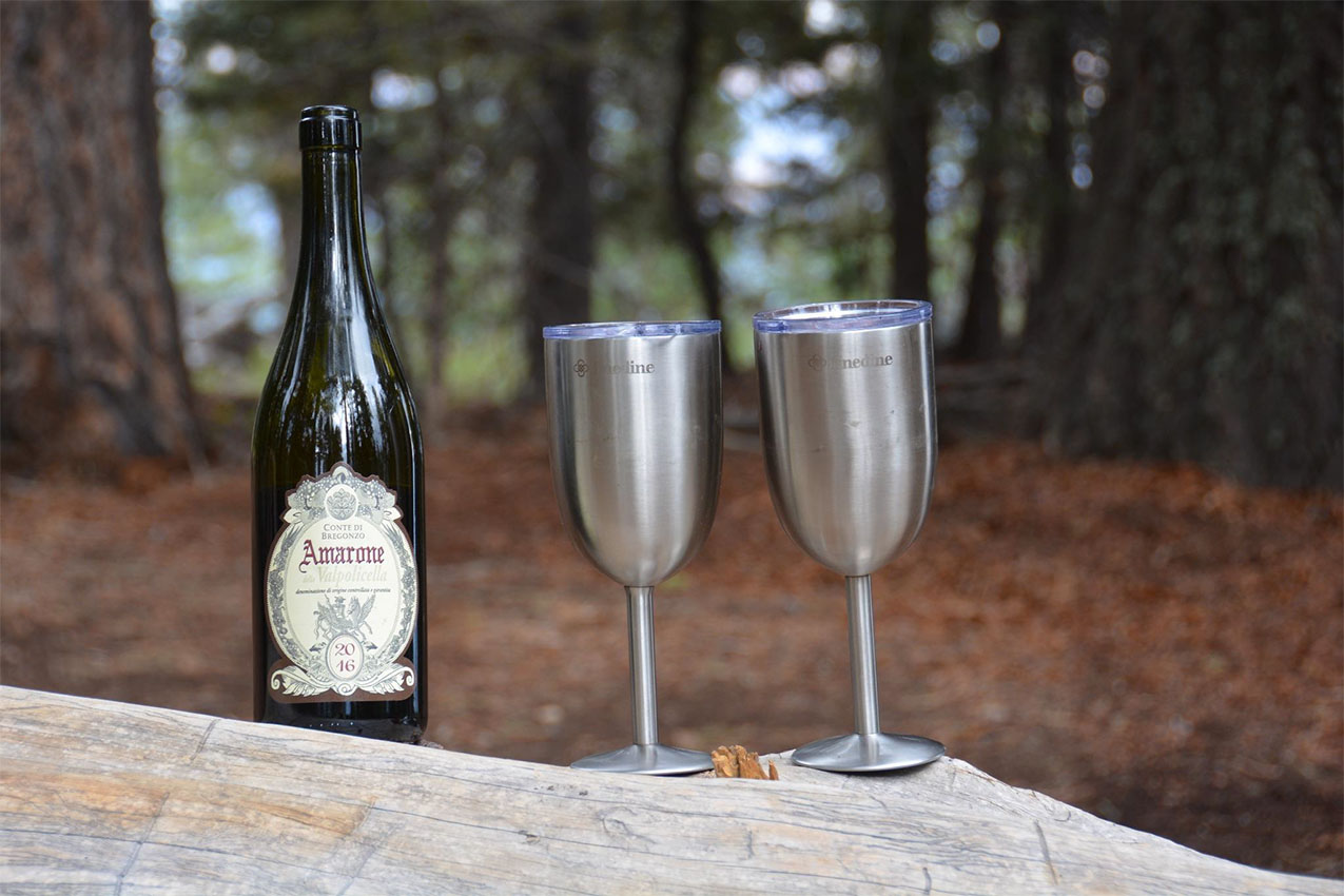 A bottle of wine and two stainless steel wine glasses.
