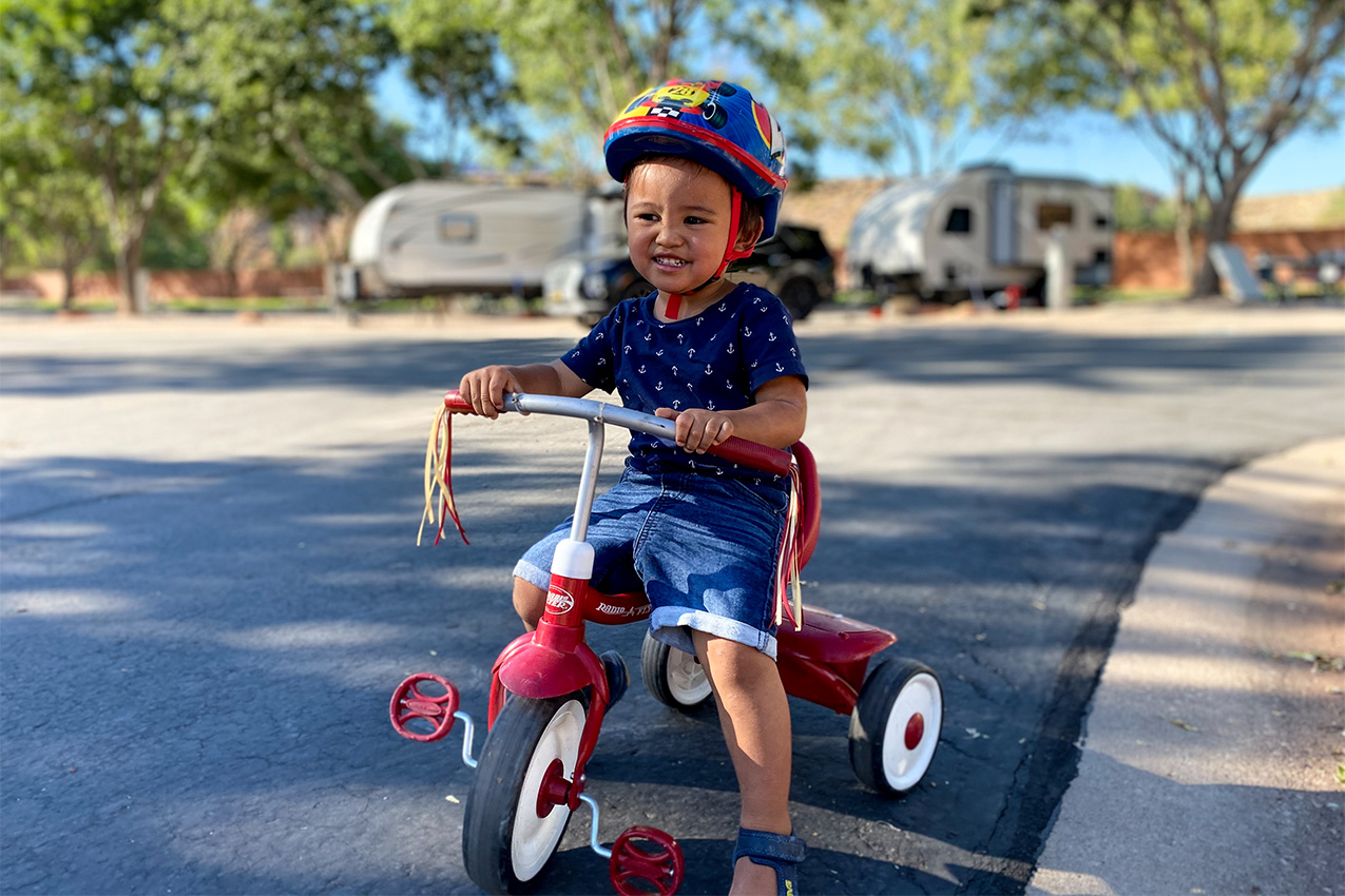 Toddler in blue shirt and shorts wearing a helmet sitting on a tricycle.
