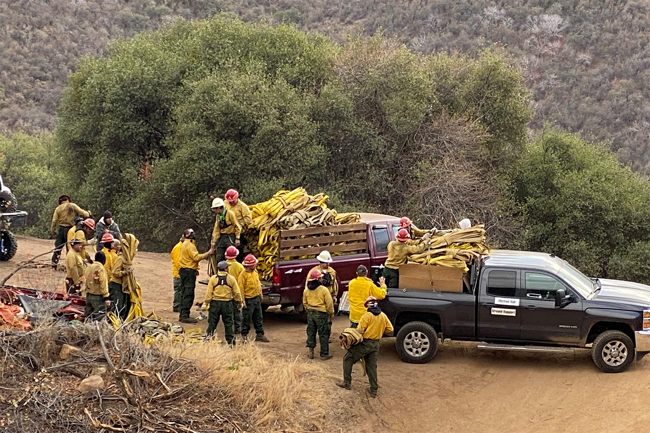 A hotshot crew standing by two trucks filled with fire hoses.