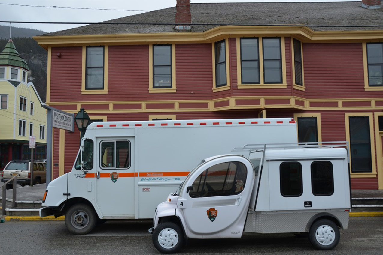 Two national park electric vehicles parked in front of a visitor center.