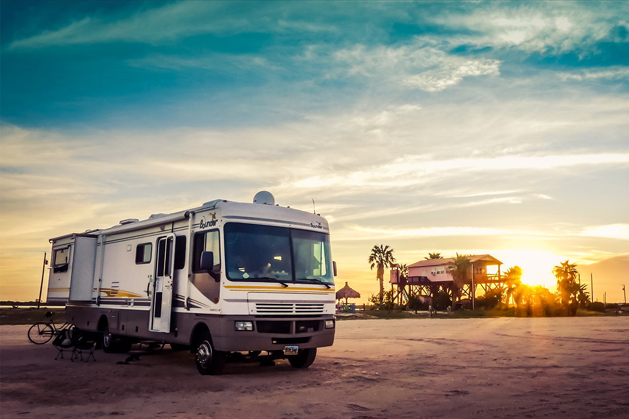 White class A parked on a beach with house on silts in the background.