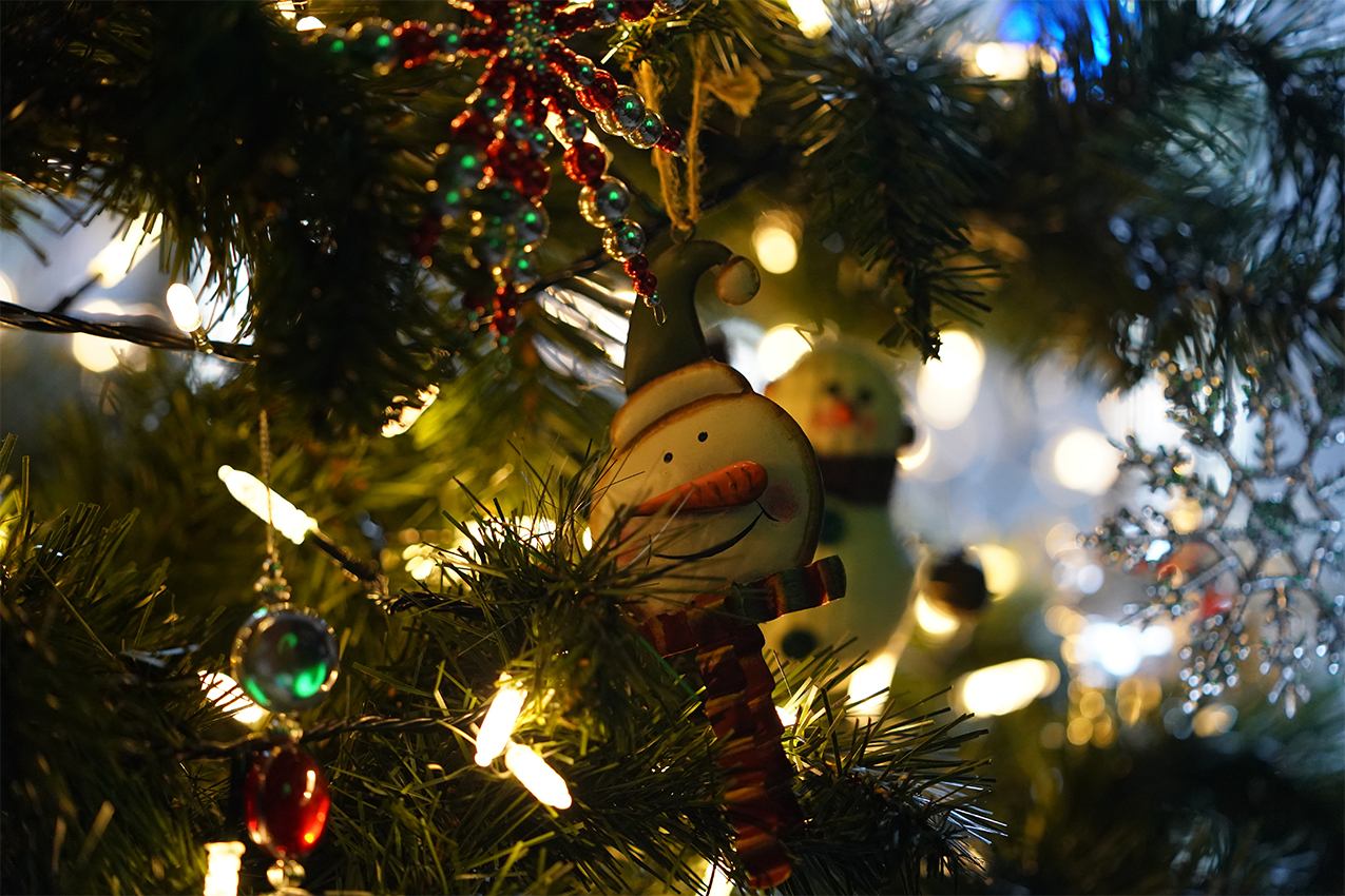 Close up photo of snowman Christmas tree ornament hanging on a lit up tree.