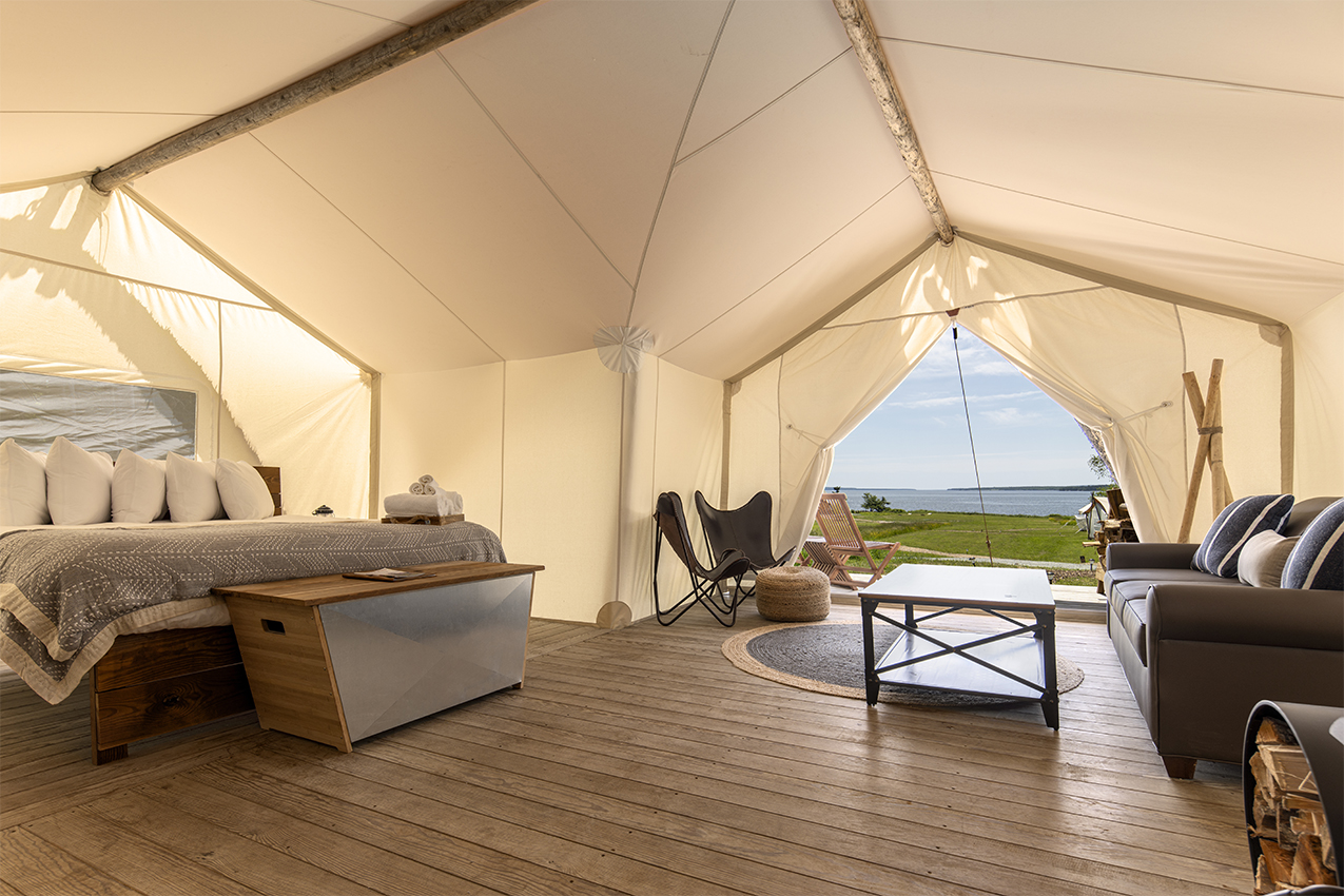 Bed, couch and coffee table inside a canvas tent looking out onto water.