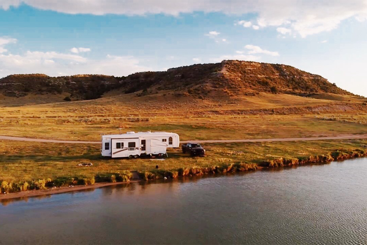 Large fifth wheel and truck parked along a shoreline.