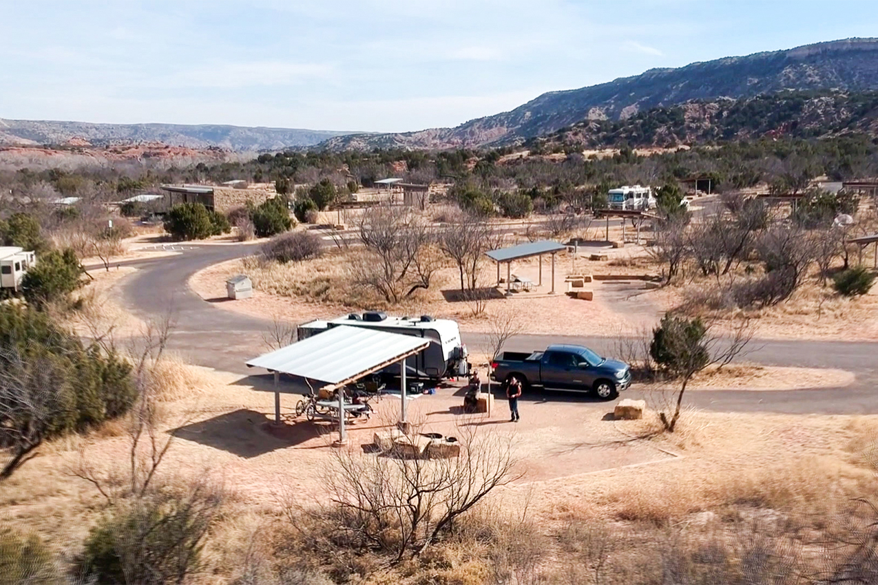 Truck and RV parked in front of a metal picnic shelter at a campground.