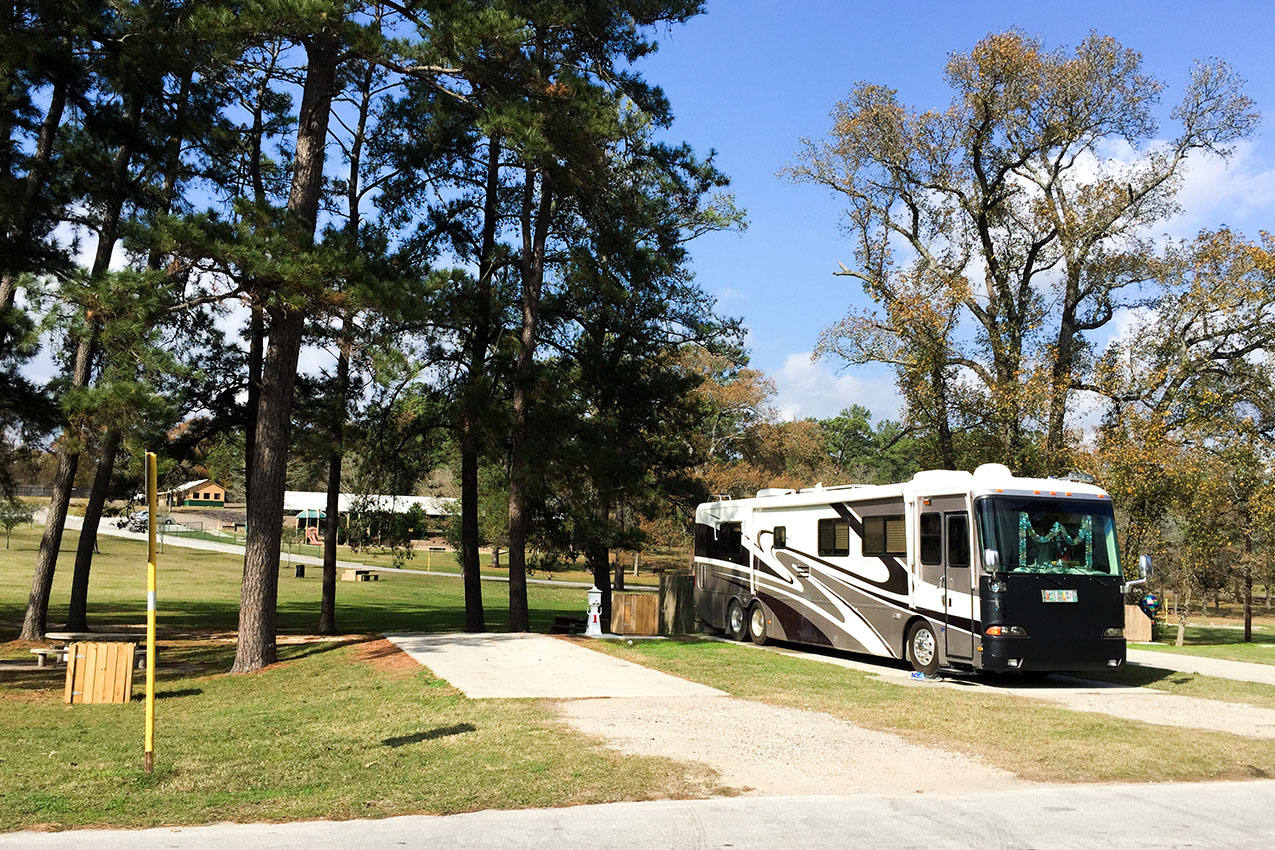 Class A parked on a concrete pad in the woods at an RV park.