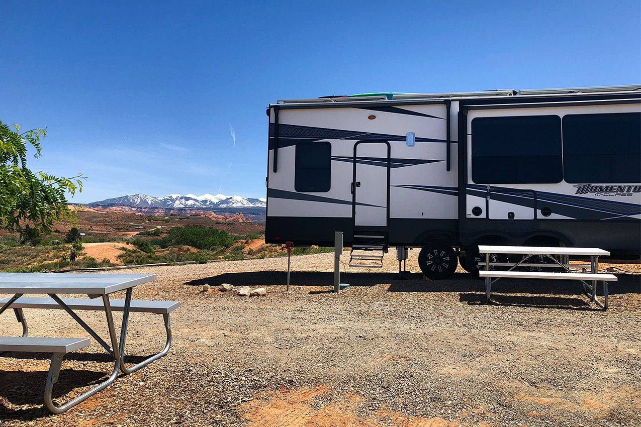RV parked in a large gravel lot in the desert with white cap mountains in the horizon.
