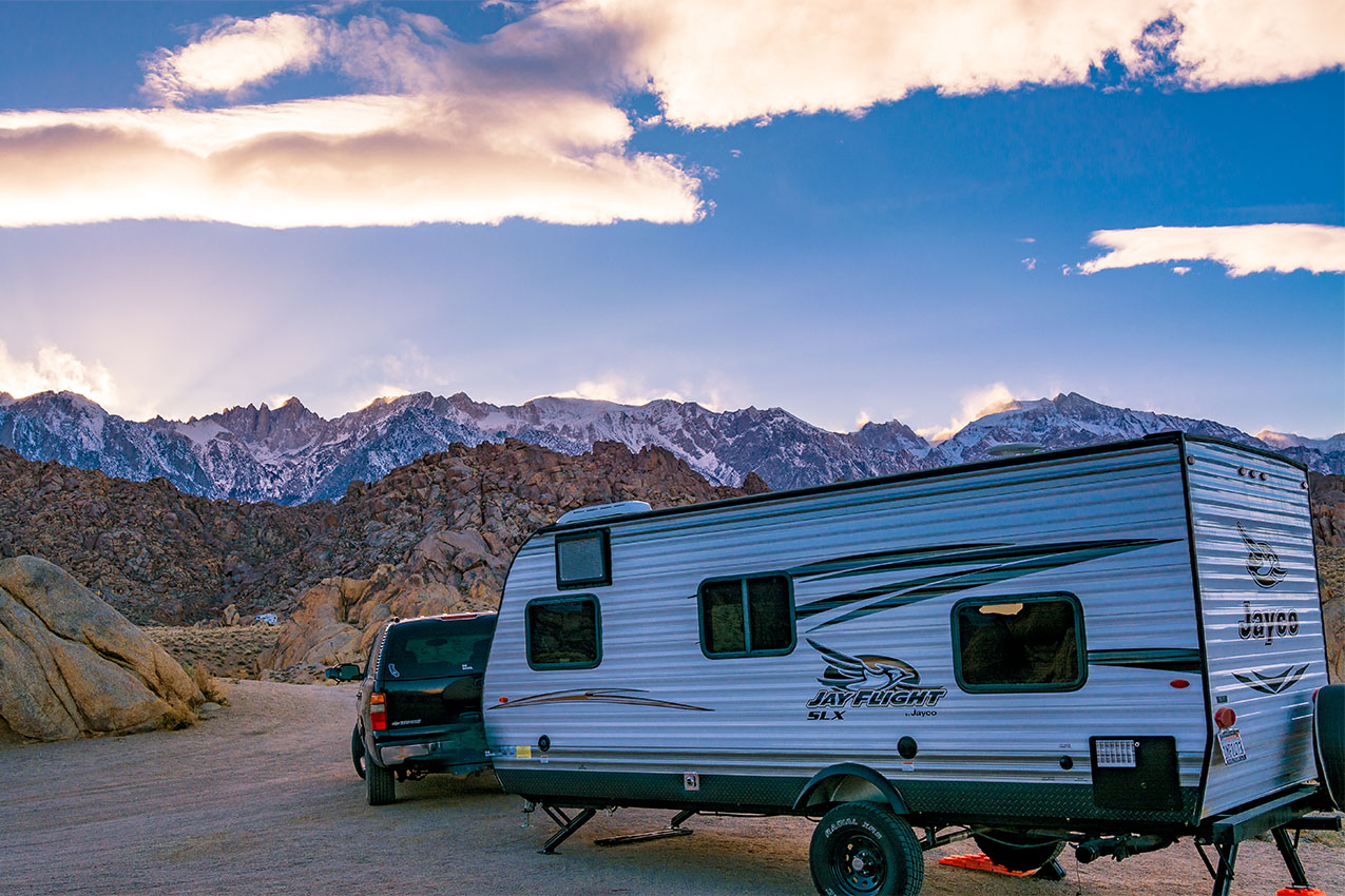 RV and trailer parked amongst rocks at sunset.
