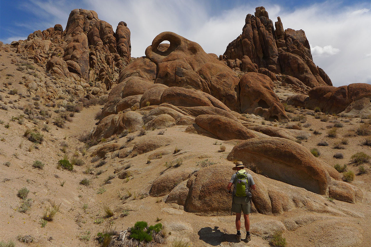 A man stands at the foot of a towering cliff formation