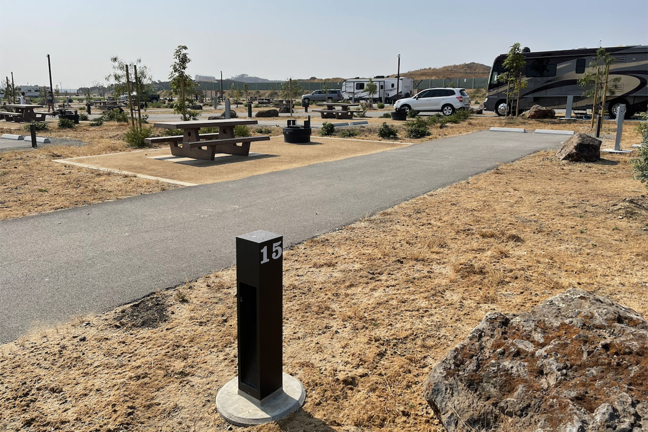 Empty paved RV site with a picnic table and fire pit next to it.