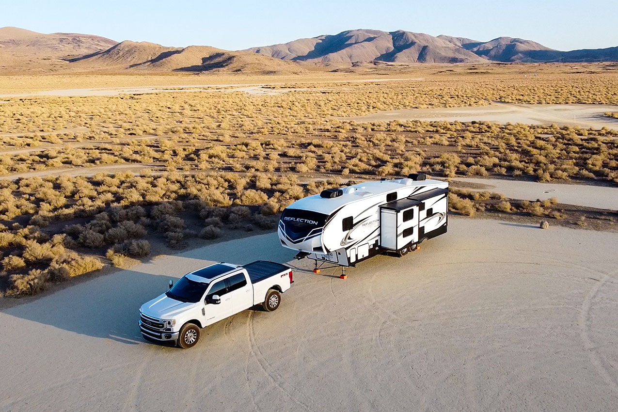 Truck and fifth wheel parked on a dry lake bed surrounded by shrubs and mountains in the background.